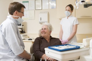 Dentist and assistant in exam room with woman in chair smiling