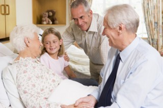 Family Sitting With Senior Woman In Hospital